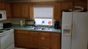 A kitchen with wooden cabinets, a microwave, a toaster, a sink, and a refrigerator. - Beach-living 2 bed (Fernandina Beach)