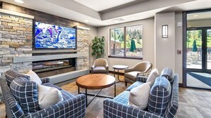 A modern lounge area with a stone wall, a flat-screen TV, comfortable seating, and a large window offering a view of the outdoors. - Luxury Windham Mtn Slope Side 3 BDRM Condo (Windham)