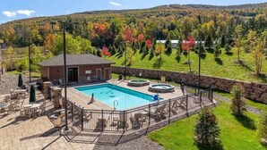 A swimming pool with a hot tub, surrounded by a stone wall and a fenced deck area with chairs and umbrellas. - Luxury Windham Mtn Slope Side 3 BDRM Condo (Windham)