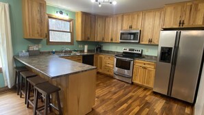 A kitchen with wooden cabinets, a stainless steel refrigerator, a microwave, an oven, and a wooden bar counter with stools.