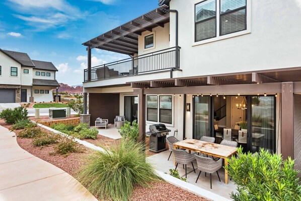 Een modern huis met twee verdiepingen, een patio, terrasmeubels en een barbecueplaats.