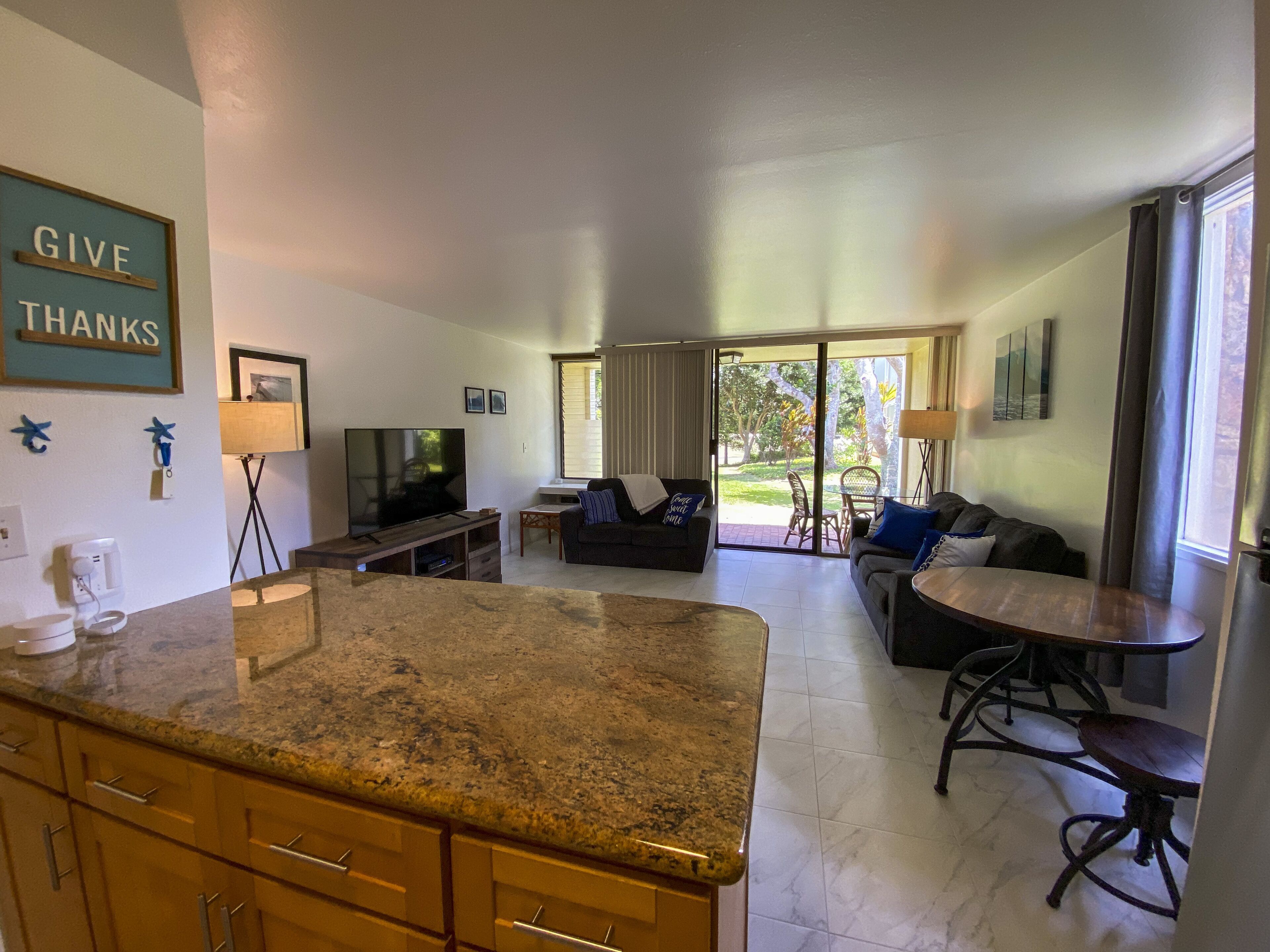 A modern living room with a large TV, a dining area, and a kitchen with granite countertops.
