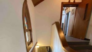 Eine Holztreppe mit Handlauf, einem kleinen Fenster und einer Tür am Obergeschoss.