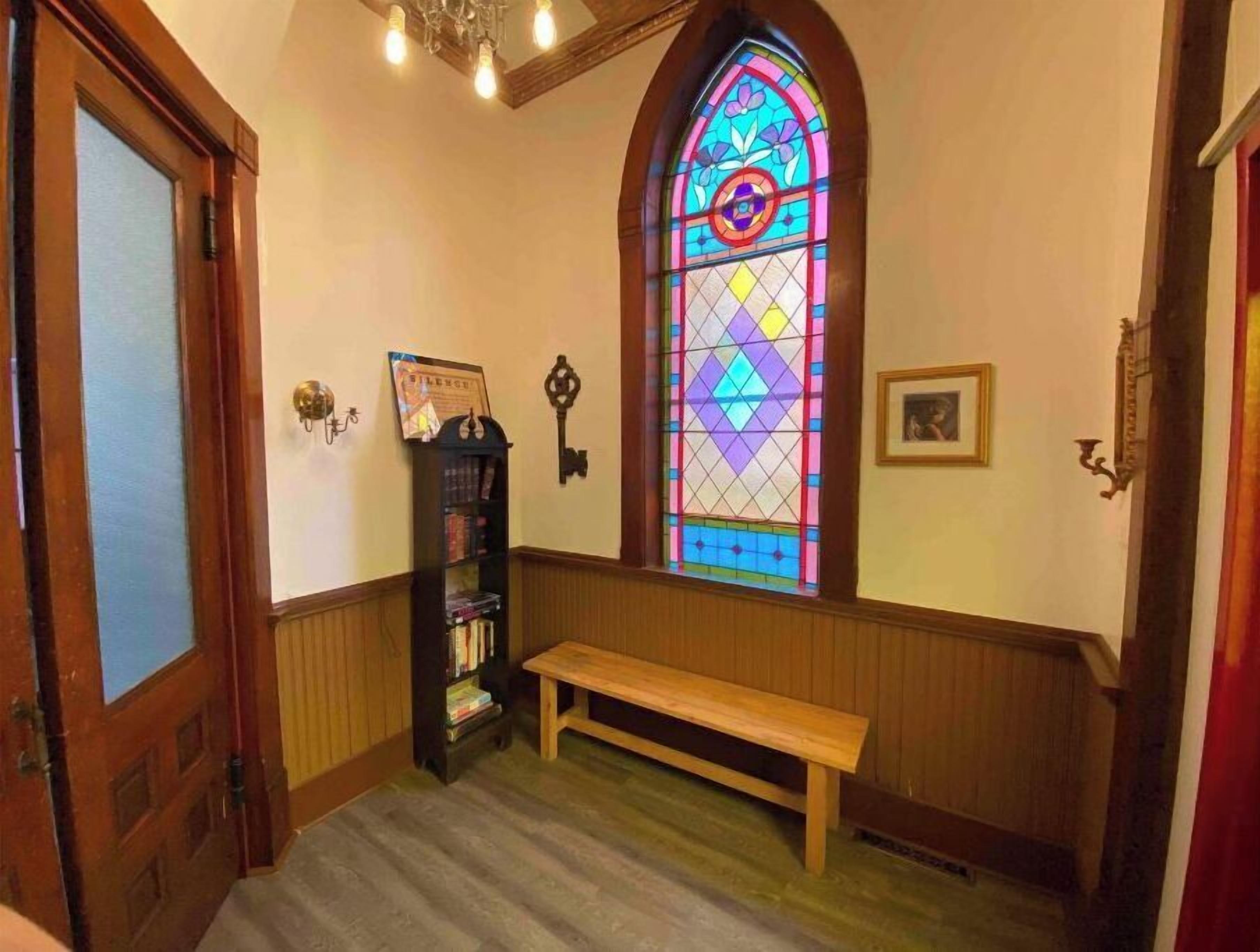 A hallway with a wooden bench, a stained glass window, a bookshelf, and a door.