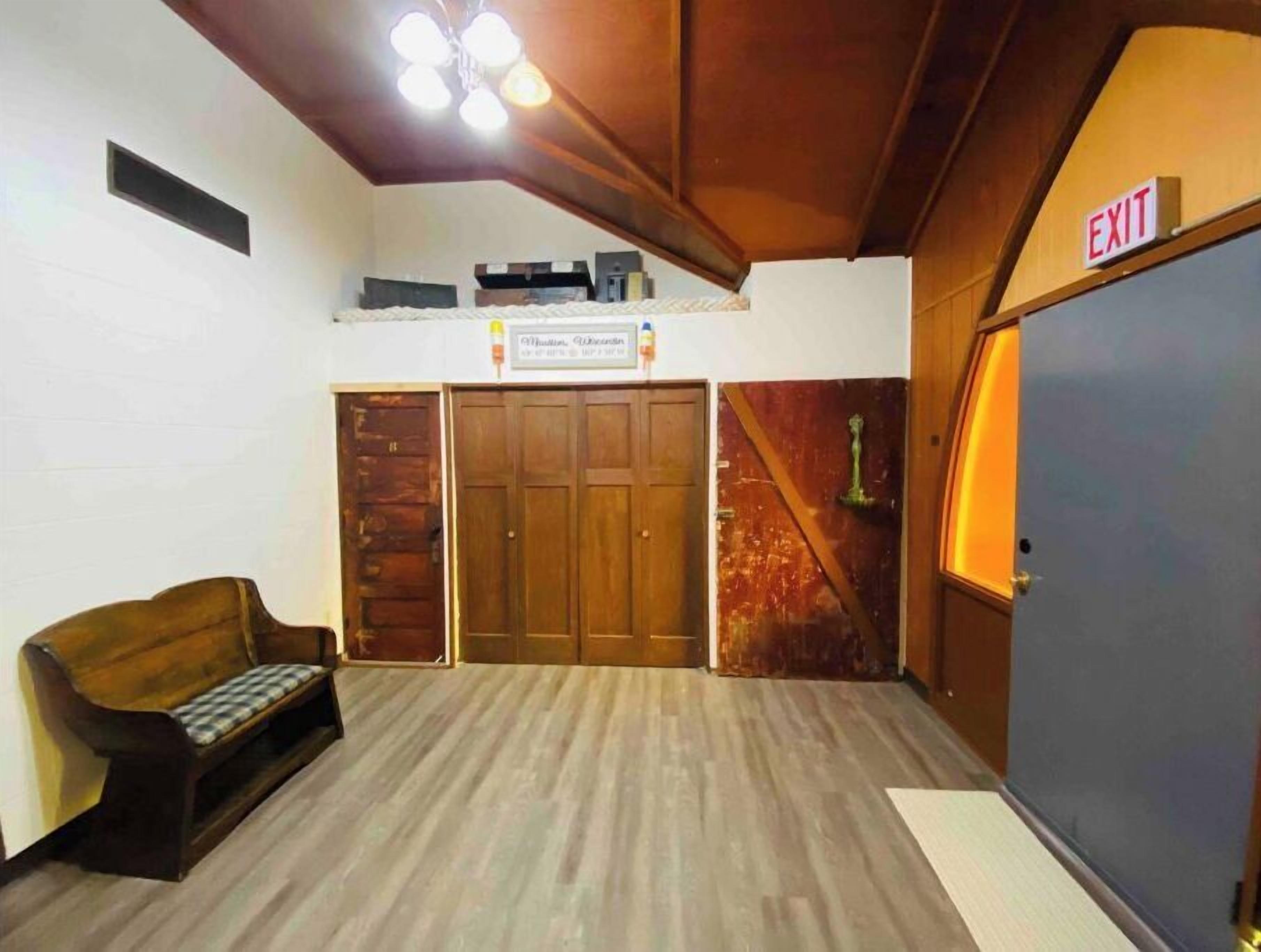 Una habitación con un banco de madera, un letrero sobre una puerta y una señal de salida.