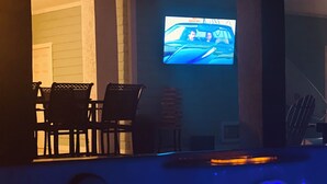 A bar area with a television displaying a scene from a movie, bar stools, and a counter with a blue light. - 3-bedroom house in Lower Keys with Hot Tub, Sleeps 10+, Pet Freindly (Big Pine Key)