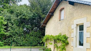 A house with a stone exterior, a small window, and a garden area with wicker furniture and a grapevine. - Cosy Cottage with pool in the countryside, France (Persac)