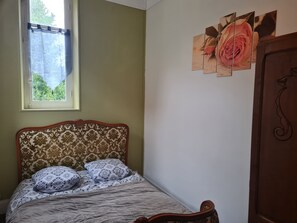 A bedroom with a bed, a window, and a wall with a floral artwork.