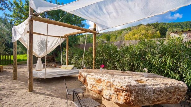 Un'area salotto esterna rustica con una panchina in pietra, un'amaca e un tettoia.