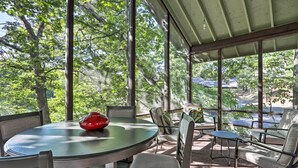 Un espacio al aire libre cubierto con una mesa redonda y sillas, ventanas amplias y vista a árboles.