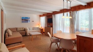 Una sala de estar acogedora con un sofá, una mesa de comedor con sillas, un televisor y una ventana con cortinas.
