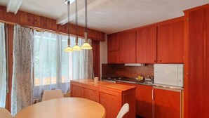 Una cocina compacta con armarios de madera, una isla central, una mesa de comedor con sillas y un refrigerador.