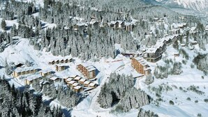 Un resort invernal cubierto de nieve con varias cabañas de estilo chalet, rodeado de densos bosques y laderas nevadas.
