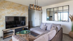 Ein modernes Wohnzimmer mit großem Flachbildfernseher, einer Steinwand, einer Couch, einem Couchtisch und einem großen Spiegel.