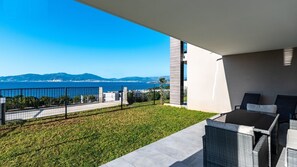 Un balcón con vistas al mar y a las montañas, una mesa con sillas y una zona ajardinada.