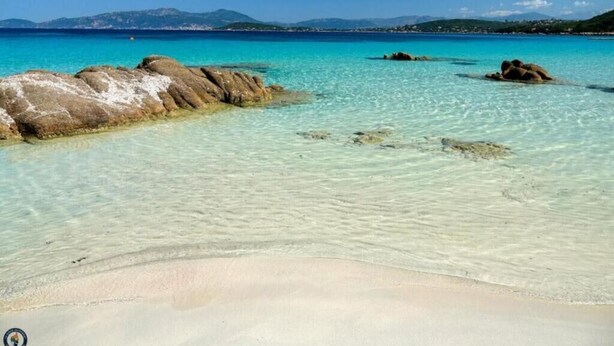 Ein sauberer Strand mit sichtbaren Felsen und einer entfernten Bergkette.