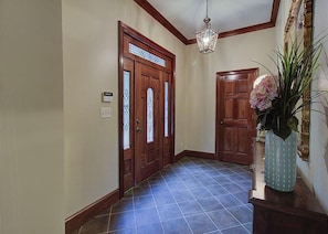 A hallway with two wooden doors, a tiled floor, a hanging light fixture, and a vase with flowers on a console table. - Burning Tree Ranch #656 (Sevierville)