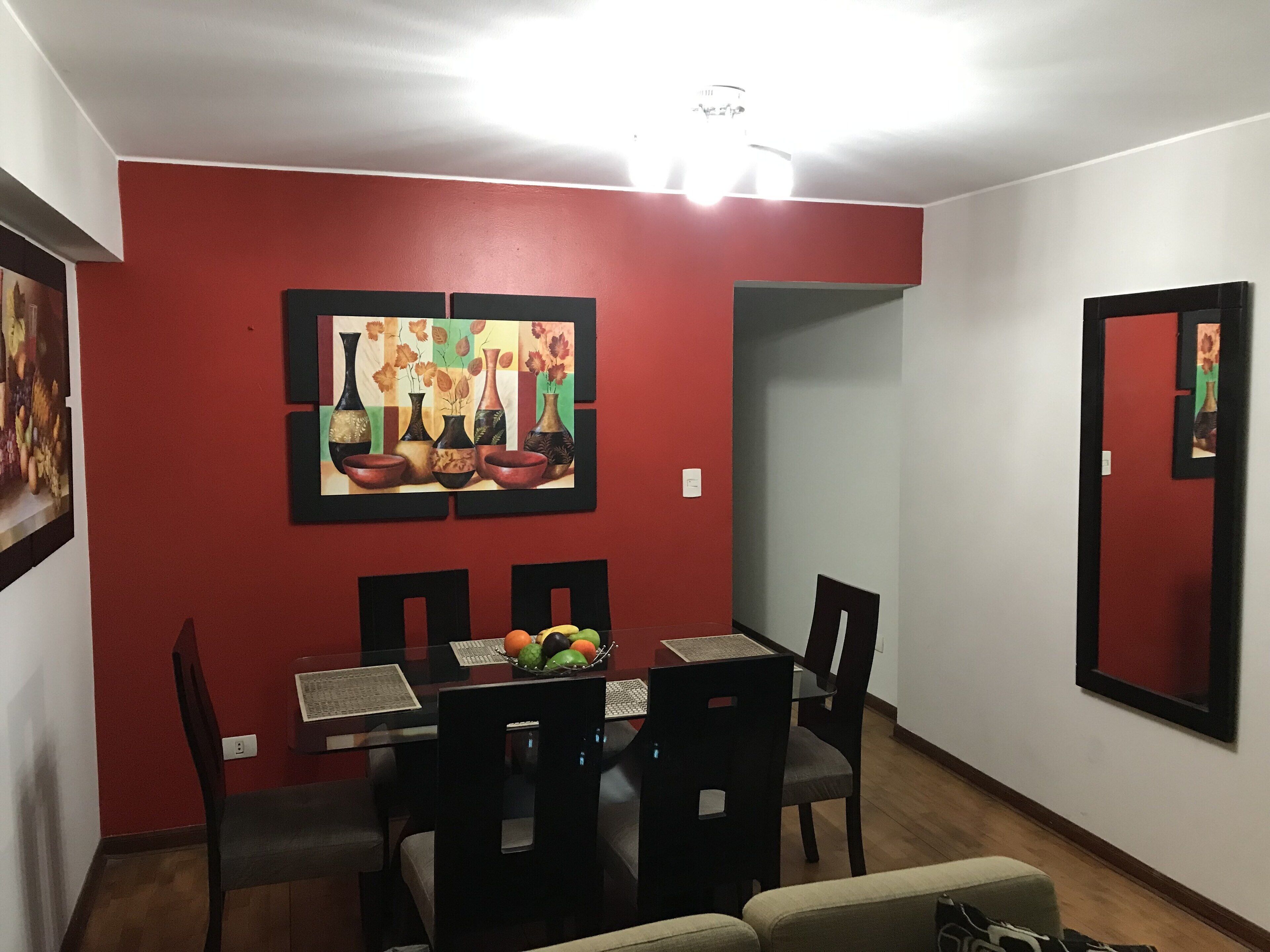 Un comedor con pared roja, un cuadro de jarrones y una mesa con sillas.