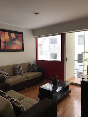 A living room with a sofa, a coffee table, and a painting on the wall. - Charming & Luxury Condo (Miraflores)