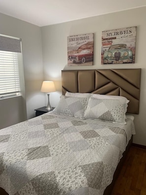 A bedroom with a quilted bedspread, a headboard with a geometric design, and two wall art pieces depicting vintage cars. - Charming & Luxury Condo (Miraflores)
