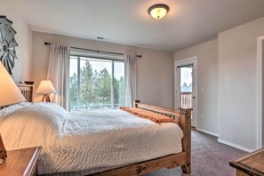 Een slaapkamer met een groot bed, een raam met gordijnen, een nachtkastje met lampen en een deur naar een andere kamer.