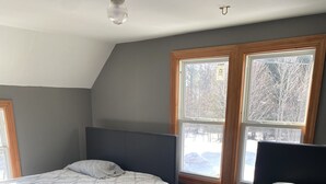 A bedroom with two beds, a small table, and large windows with a view of trees. - Gateway to the Keweenaw  (Allouez)