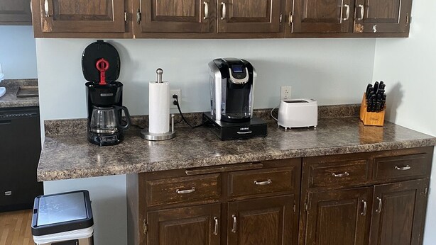 A kitchen with wooden cabinets, a granite countertop, a coffee maker, a toaster, and a trash bin. - Gateway to the Keweenaw  (Allouez)