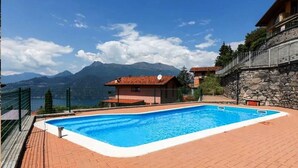 Une piscine avec vue sur les montagnes, un mur en pierre et un bâtiment au toit rouge.