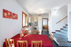 A dining area with a red tablecloth, wooden chairs, and a vase. A kitchen with white cabinets and a stove is visible in the background. - Pet-Friendly Villa Magic Moment in Lake Como with Lake View, Pool, Wi-Fi, Terrace & Garden (Perledo)