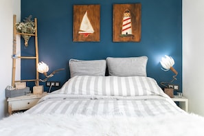 Une chambre à coucher comprenant un lit, deux oreillers, une table de chevet, une lampe et deux œuvres d’art murales.