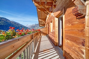 A wooden balcony with a view of mountains and flowers.