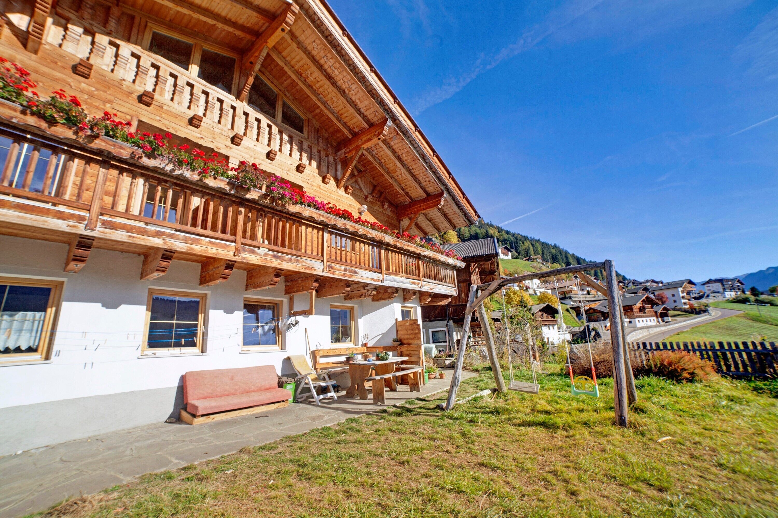A wooden chalet with a balcony, a patio with a table and chairs, and a view of the surrounding landscape.