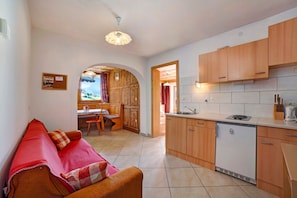 A compact kitchen with wooden cabinets, a built-in dishwasher, and a dining area with a table and chairs.