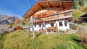 A wooden chalet with a balcony, a wooden deck, and a mountain backdrop.