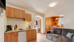 A compact kitchen with wooden cabinets, a built-in dishwasher, and a dining area with a grey sofa.