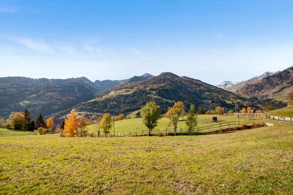 Un paisaje montañoso con cielo despejado, un campo cercado y colinas distantes.