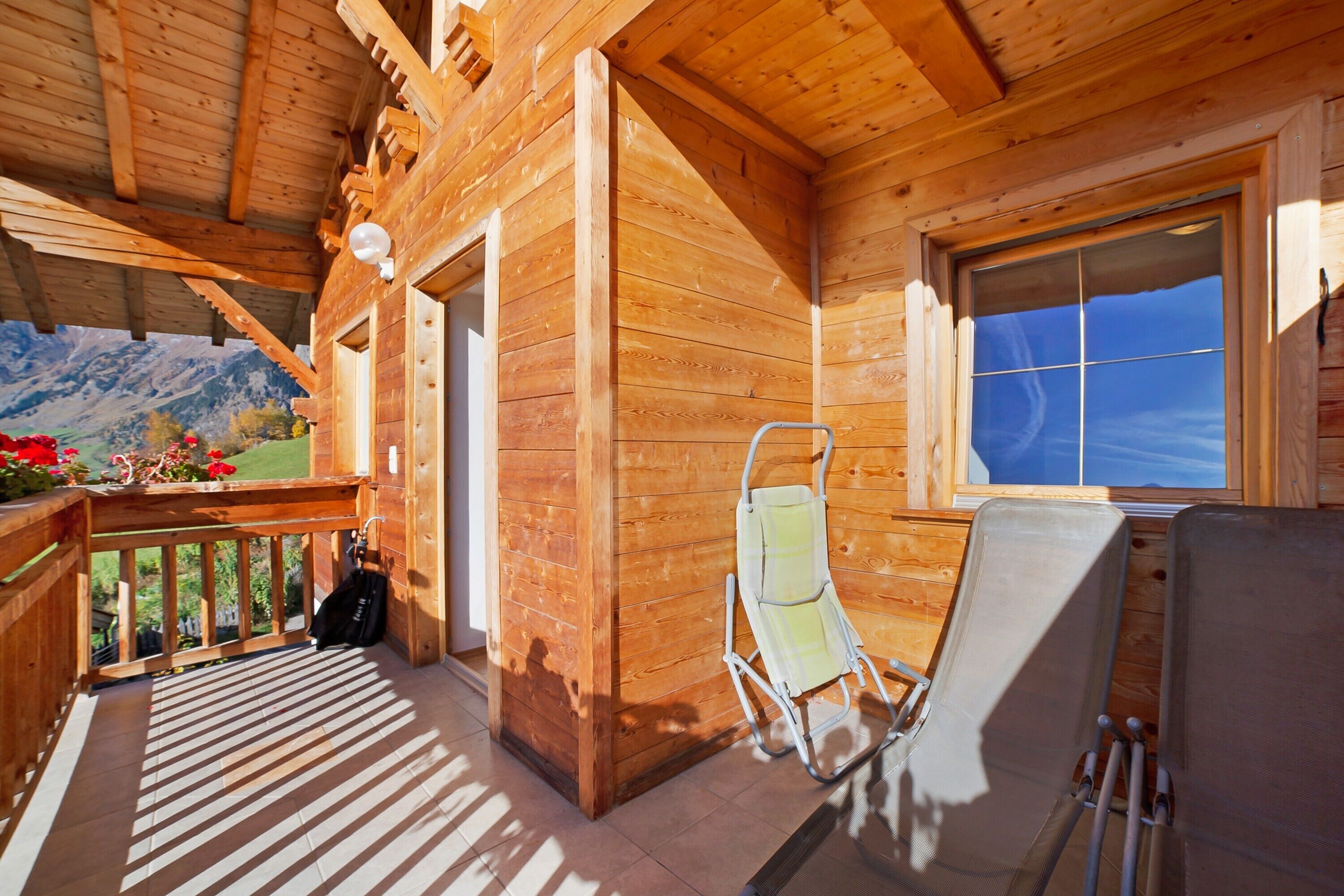 En træhytte med balkon, stol og vindue med udsigt til et bjerg.