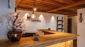 A wooden reception desk with a vase of orchids, a hanging light fixture, and a wall sign reading 'Sassella'.