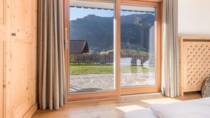 A room with a wooden floor, a sliding glass door leading to a balcony, and a view of a mountainous landscape. - Apartment 'Cesa Sassela 2' with Mountain View, Sauna, Pool, Garden & Wi-Fi (Ortisei)