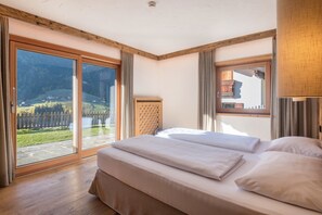 Quarto com uma grande porta de vidro deslizante, cama com roupa de cama branca e teto de madeira.