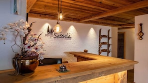Um balcão de recepção de madeira com um vaso de orquídeas, um lustre pendente e uma placa na parede com a inscrição 'Sassella'.