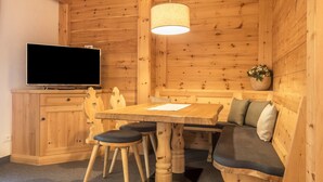A wooden interior with a TV, wooden dining table, chairs, a bench, and a hanging light fixture. - Apartment 'Cesa Sassela' with Mountain View, Sauna, Pool, Garden, Balcony & Wi-Fi (Ortisei)