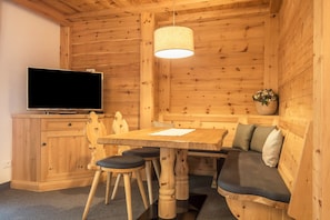 A wooden interior with a TV, wooden dining table, chairs, a bench, and a hanging light fixture.