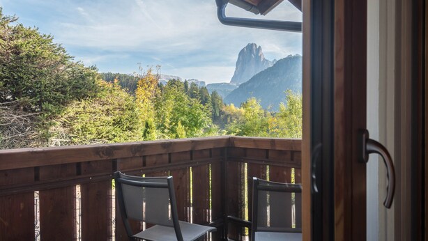 A balcony with two chairs, a wooden railing, and a view of a mountainous landscape. - Apartment 'Cesa Sassela' with Mountain View, Sauna, Pool, Garden, Balcony & Wi-Fi (Ortisei)