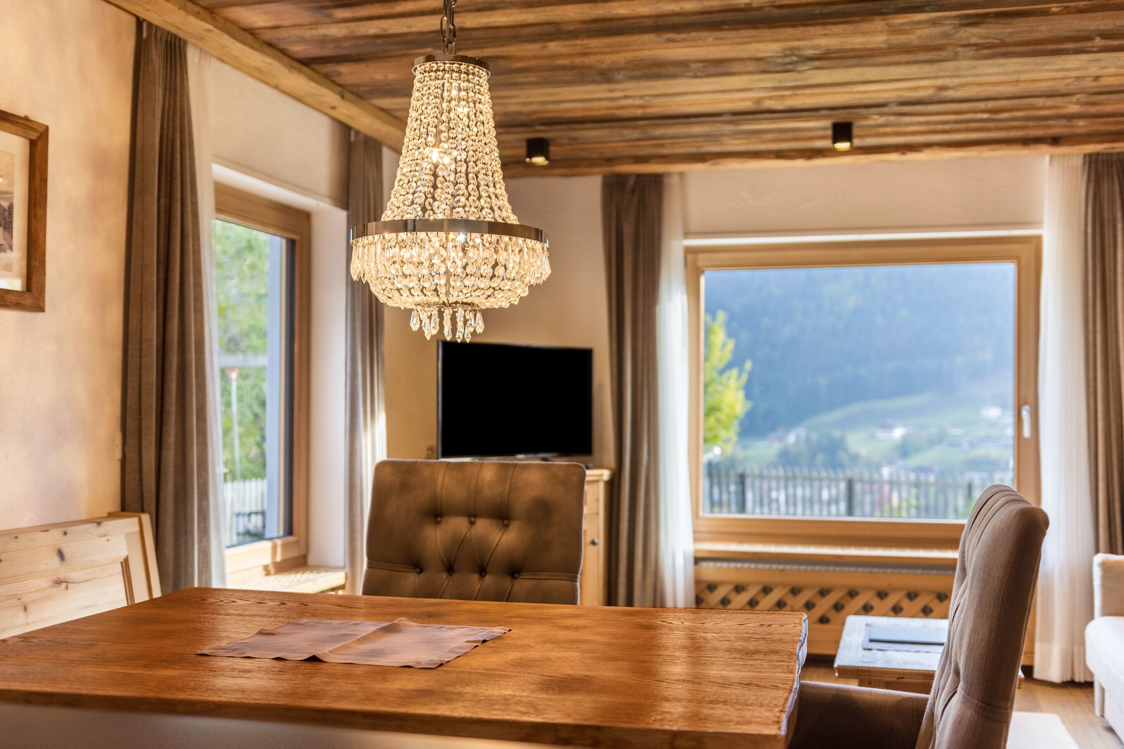 A dining area with a wooden table, a chandelier, and a view of a mountainous landscape through large windows.