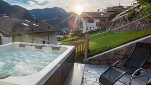 A hot tub with a view of a mountainous landscape and a wooden deck. - Apartment 'Cesa Sassela Relax' with Mountain View, Sauna, Pool, Garden, Balcony & Wi-Fi (Ortisei)