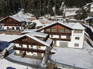 A snow-covered resort with wooden buildings, a stone wall, and a fenced area.