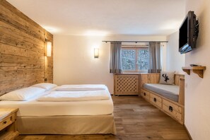 A room with a wooden wall, a bed with two pillows, a TV mounted on the wall, and a window with curtains.