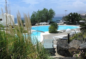 A pool area with lounge chairs, a view of the ocean, and a mountainous backdrop.