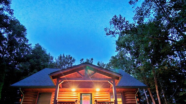 A log cabin with a porch, a front door, and a staircase leading up to the entrance.